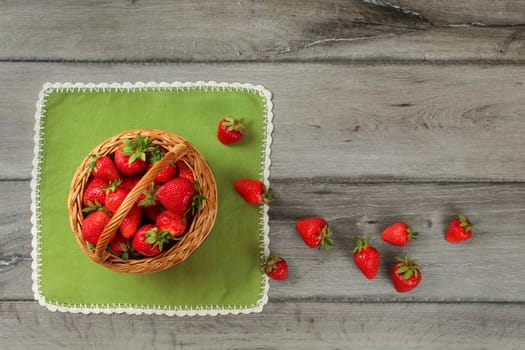 Tabletop photo, basket with strawberries , some of them spilled on green tablecloth and gray wooden desk.