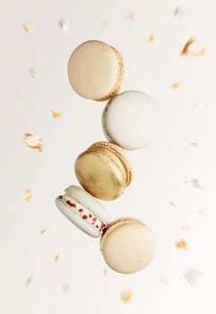 White, yellow, gold macaron cookies. Colorful, sweet small French macaroon cakes. Light beige blurred background with broken macaron cuts, bits, bitten parts. Five cookies in the center of photo