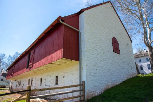 Beautiful dramatic image of early American agricultural scene with large stone bak barn made of whitewashed stone and red wood with shuttered window and barnyard with rural background and copy space. No people.