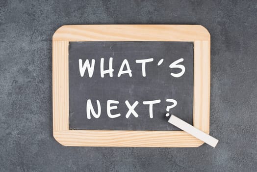 The phrase what´s next is standing on a chalkboard, having new goals and strategies, making plans for future