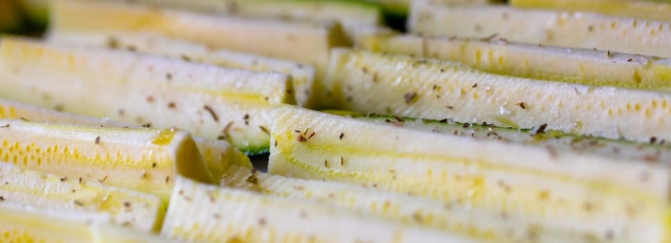 Panorama banner of fresh seasoned zucchini slices or courgettes ready for oven roasting sprinkled with aromatic herbs in a low angle full frame view