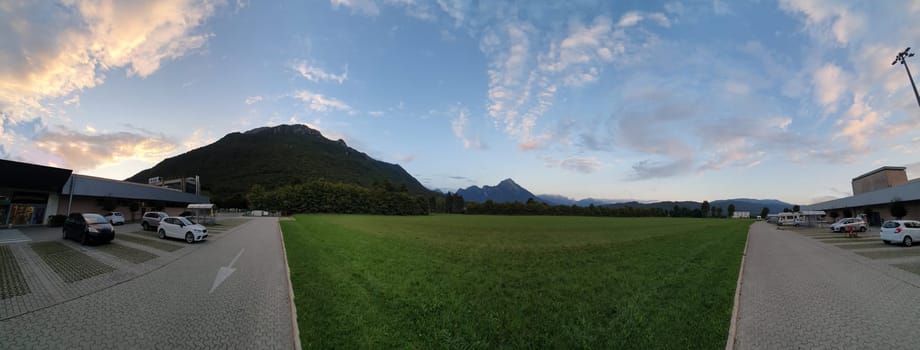 panoramic view of a modern mountain town in northeastern Italy, with the blue sky mottled with clouds and a beautiful green lawn