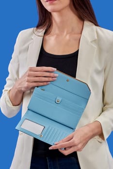 A beautiful young woman is holding a blue purse on a blue background. High quality photo