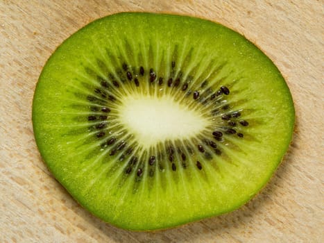 Single slice of juicy kiwi fruit sitting on a wood cutting board.