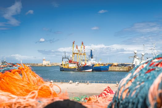Large fishing boats moored in Howth harbour seen through blurred nets. Phishing and shellfish fishing equipment on fishing boats, Dublin, Ireland