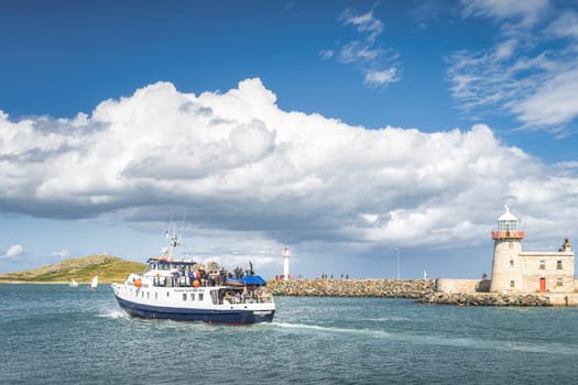 Dublin, Ireland, Aug 2019 Group of people, tourists on a tour boat in Howth marina with Howth Lighthouse and Irelands Eye island in the background
