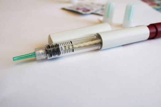 Injection syringe on a white table with spare needles in the background. Diabetes mellitus..