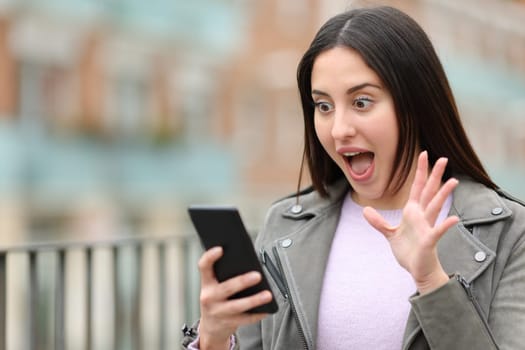 Surprised woman checking cell phone in the street