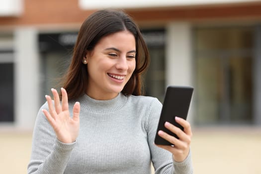 Happy teen greeting during a videocall in the street