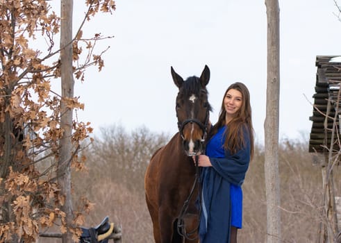 A girl in a blue dress and a horse on the background of a winter forest