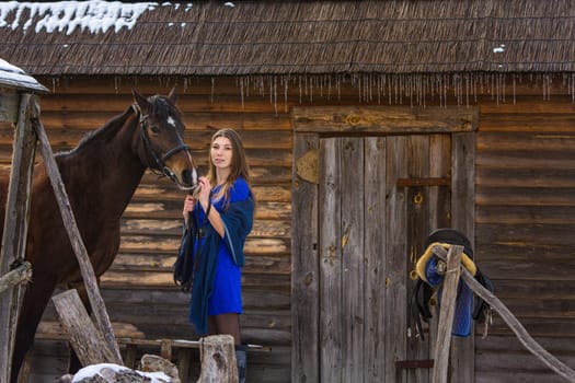 A girl stands with a horse against the background of an old wooden house
