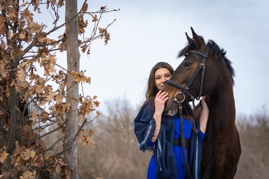 The girl peeks out from behind the muzzle of a horse, in the background an autumn forest