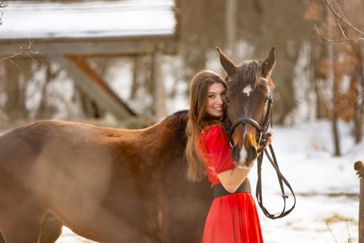 A beautiful girl in a red dress hugs a horse in the rays of the setting sun