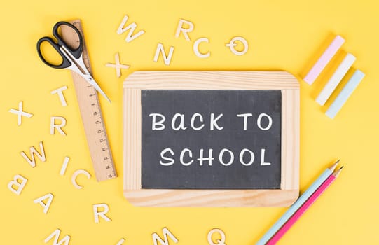 Empty chalkboard with colorful chalk, pencils, ruler, letters and a scissor, back to school and education concept