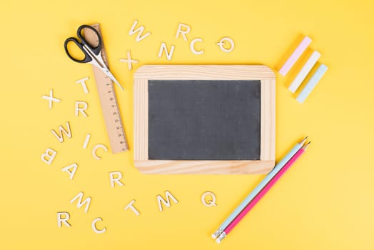 Empty chalkboard with colorful chalk, pencils, ruler, letters and a scissor, back to school and education concept