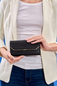 A beautiful young woman is holding a black handbag on a blue background. High quality photo