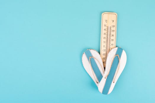 Empty blue background with a thermometer and flip flops, holiday background, summer vacation, hot weather, beach items
