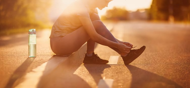 Woman sitting on the border of the roadside after a run. Panoramic view. Concept of the healthy lifestyle.