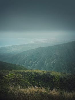 Scenery view from the top of the mountains to the ocean coastline in Hawaii, Oahu island. Moody hiking landscape with foggy, green hills on the horizon and stormy clouds over the bay