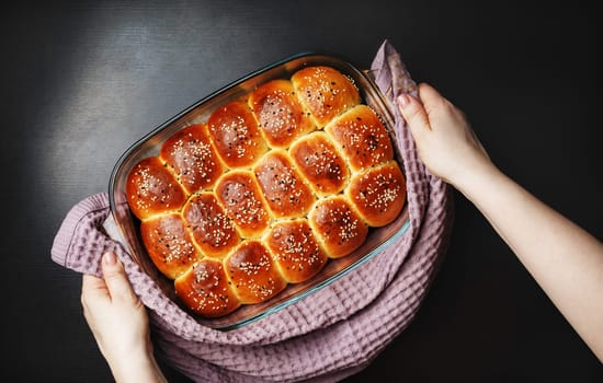 Freshly baked delicious sweet buns with sesame seeds in female hands. Flat lay.