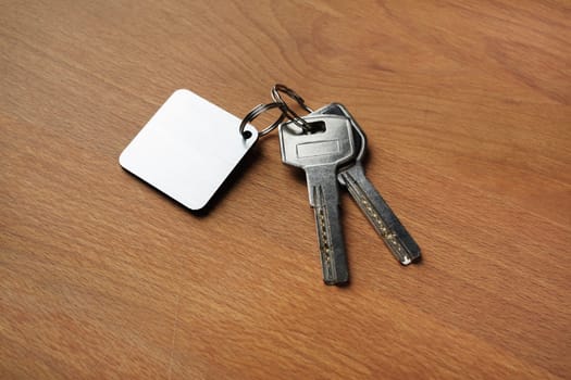 Two house keys and keychain on wooden background.