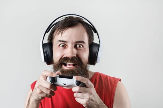 Happy bearded man in headphones and with a gamepad in his hands. Gamer plays video games.