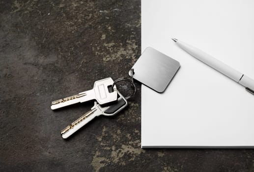 House keys, blank keychain, pen and paper on concrete background.