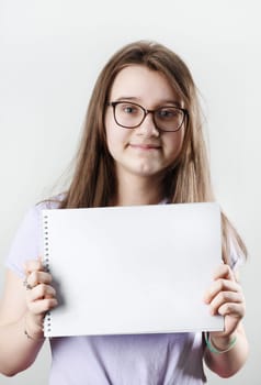 Teen girl wearing glasses showing blank sketchbook. Education concept.