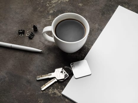 Keys, coffee cup, pen, clips and paper on concrete background.