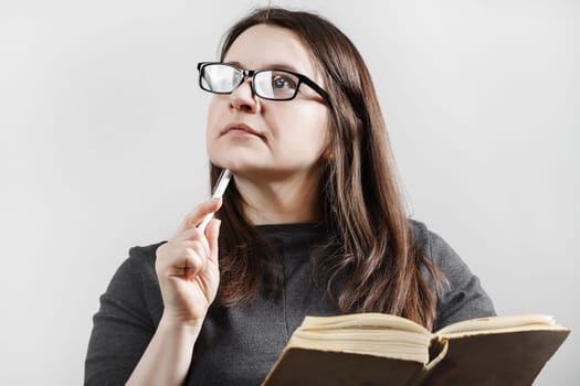 Thoughtful dreamy brunette woman in glasses reading a book. Female works on book review.
