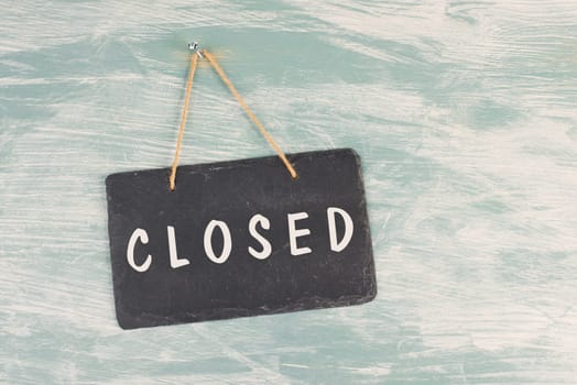 The word closed is standing on a chalkboard sign, hanging on a blue textured weathered door, concept for business, stores and restaurants