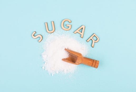 Heap of refined sugar, unhealthy food and lifestyle, ingredients for baking, wooden shovel, isolated on a blue colored background