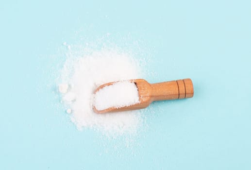 Heap of refined sugar, unhealthy food and lifestyle, ingredients for baking, wooden shovel, isolated on a blue colored background