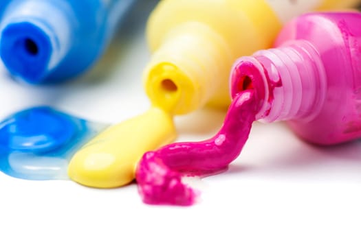 Close-up of three open tubes with magenta, yellow and blue artist paints spilling out on a white background.