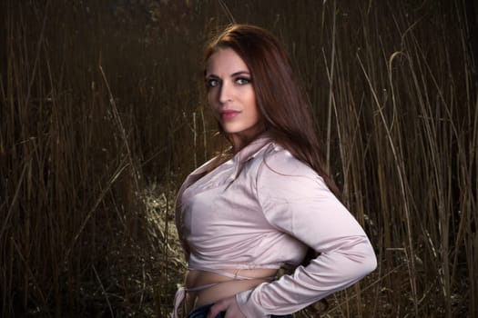 young woman in nature hay field long hair make-up country girl with hand on hip