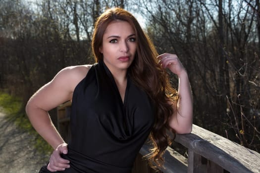 young woman standing outside posing in nature spring park wearing black dress