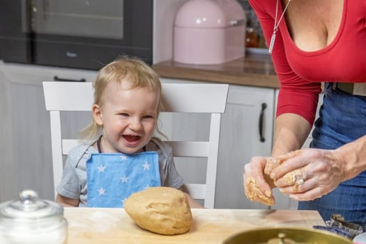 Smiling adorable funny blond little child boy is baking cake in domestic kitchen. Horizontally.