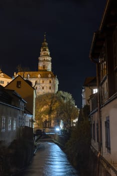 Castle of Cesky Krumlov at night. The slow flowing river Vltava is in the foreground. Vertically.