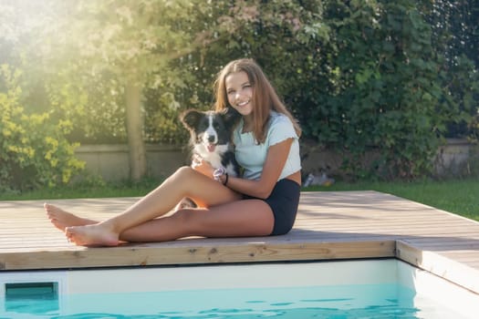 Smiling tanned girl is posing by the pool with her dog. Horizontally.