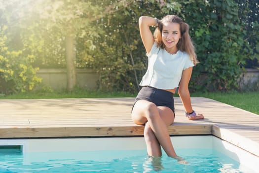 Cute tanned girl is posing with feet in the pool. Horizontally.