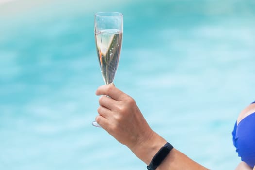 Woman is holding champagne glass in the pool closeup.  Horizontally.