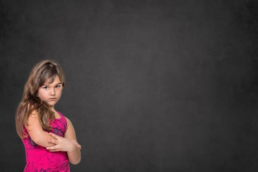 Serious long haired little girl is posing on the dark background. Horizontally.