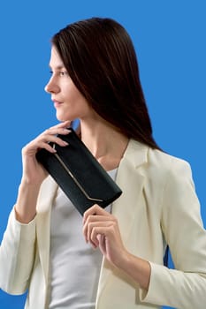 A beautiful young woman is holding a black handbag on a blue background. High quality photo