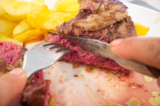 Eating grilled veal tenderloin with foie au gratin. Hands cutting meat with knife and fork