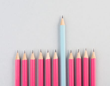 Pink pencils in a row, one blue pen is standing out, be different, leadership and teamwork concept