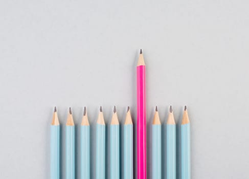 Blue pencils in a row, one pink pen is standing out, be different, leadership and teamwork concept