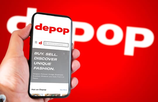 Roncade, Italy, May 2022: Depop company’s website on a phone screen. Red background with Depop logo blurred. Illustrative editorial. Selective focus. Depop is a peer-to-peer social e-commerce company