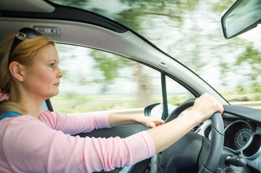 Profile portrait of serious calm woman careful and safe driving car on country road. Stock photo captured in active dynamic motion on high speed with slow shutter and blurred background.