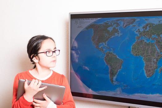 Little cute girl using at home a Tablet PC and an interactive television for homework
