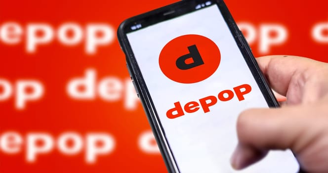 Roncade, Italy, May 2022: Male hand holding a phone with Depop company web page on screen. In the background the logo Depop blurred and repeated. Depop is a peer-to-peer social e-commerce company